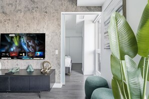 A modern living room with a flat-screen TV mounted on a textured wall, a dark console table, and a large green plant. - Charming 2BR downtown condo with private patio Parking Available (Toronto)