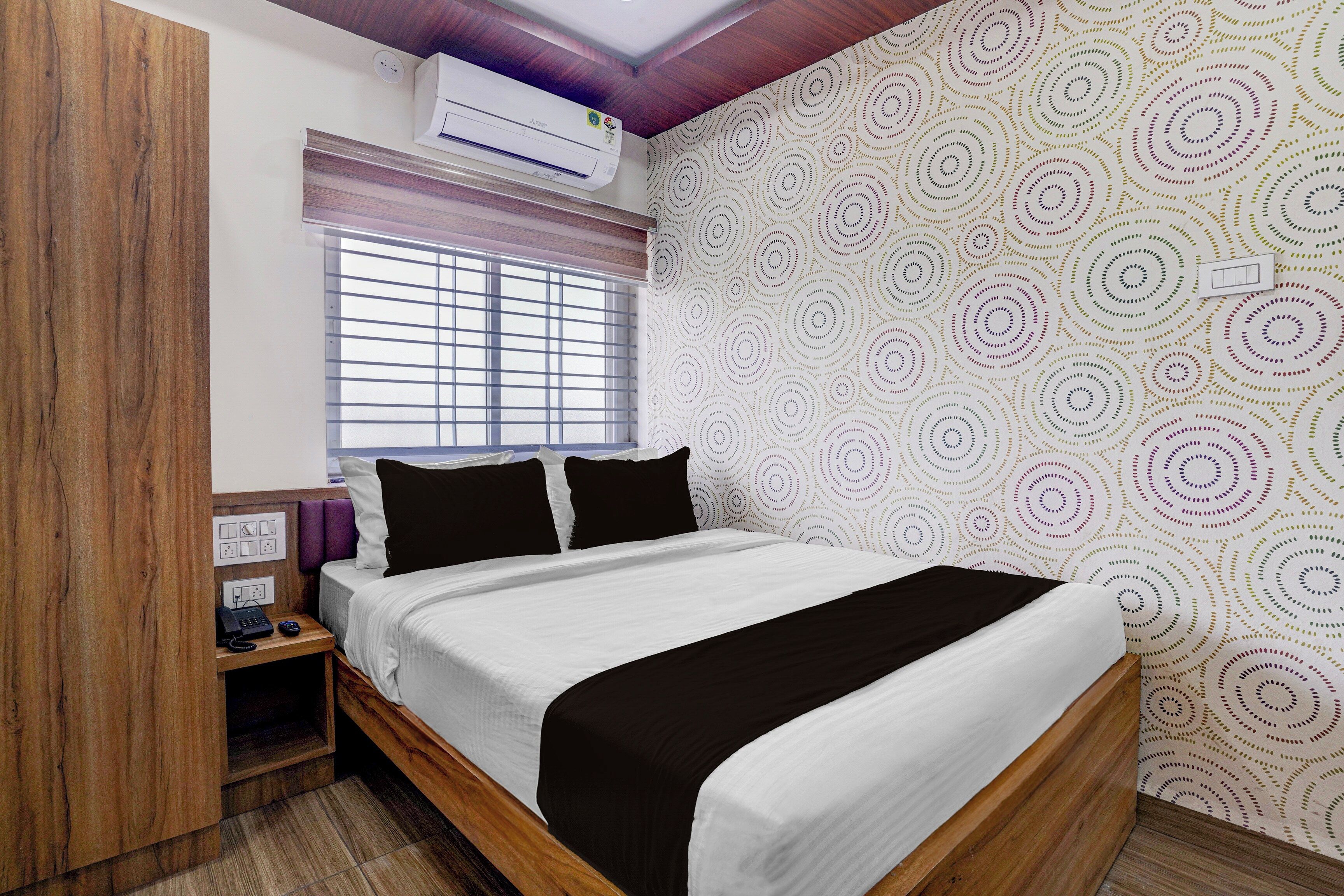 A bedroom with a bed, a nightstand, an air conditioning unit, and a window with blinds.