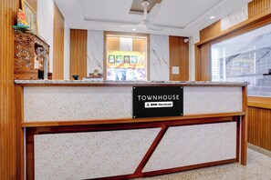 A reception desk with a marble top, a sign reading 'TOWNHOUSE' and 'OYO-Serviced', and a ceiling fan above. - Townhouse KMF Dharwad (Dharwad)