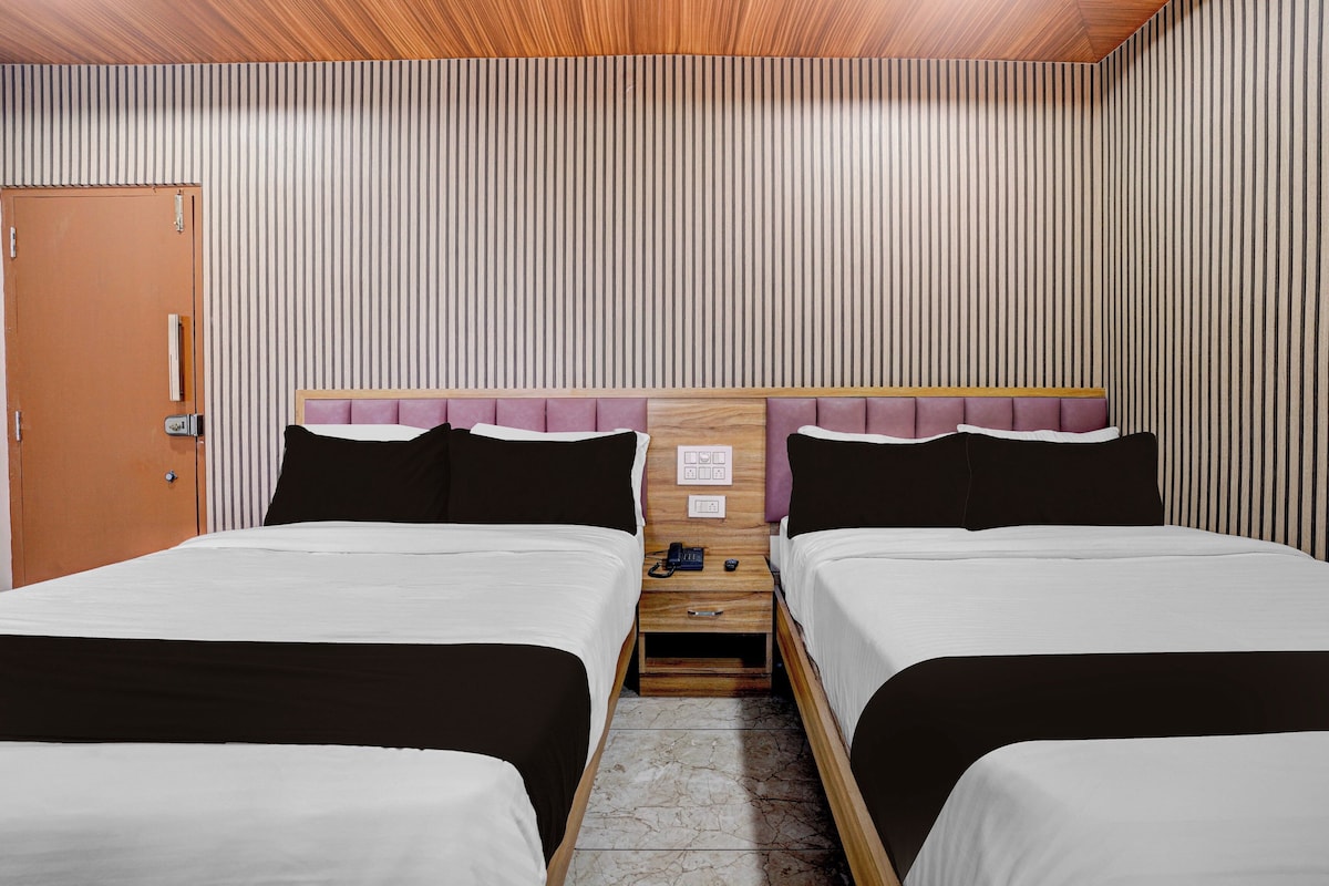 A hotel room with two beds, a wooden headboard, a nightstand with a phone, and a door.