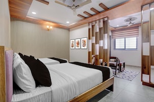 Habitación de hotel con dos camas, ventilador de techo, iluminación empotrada, ventana con persianas y un panel decorativo en la pared.