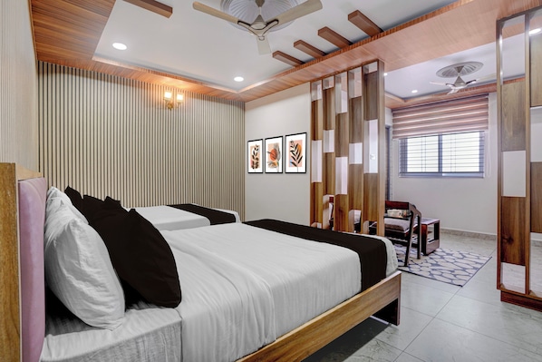 Habitación de hotel con dos camas, ventilador de techo, iluminación empotrada, ventana con persianas y un panel decorativo en la pared.