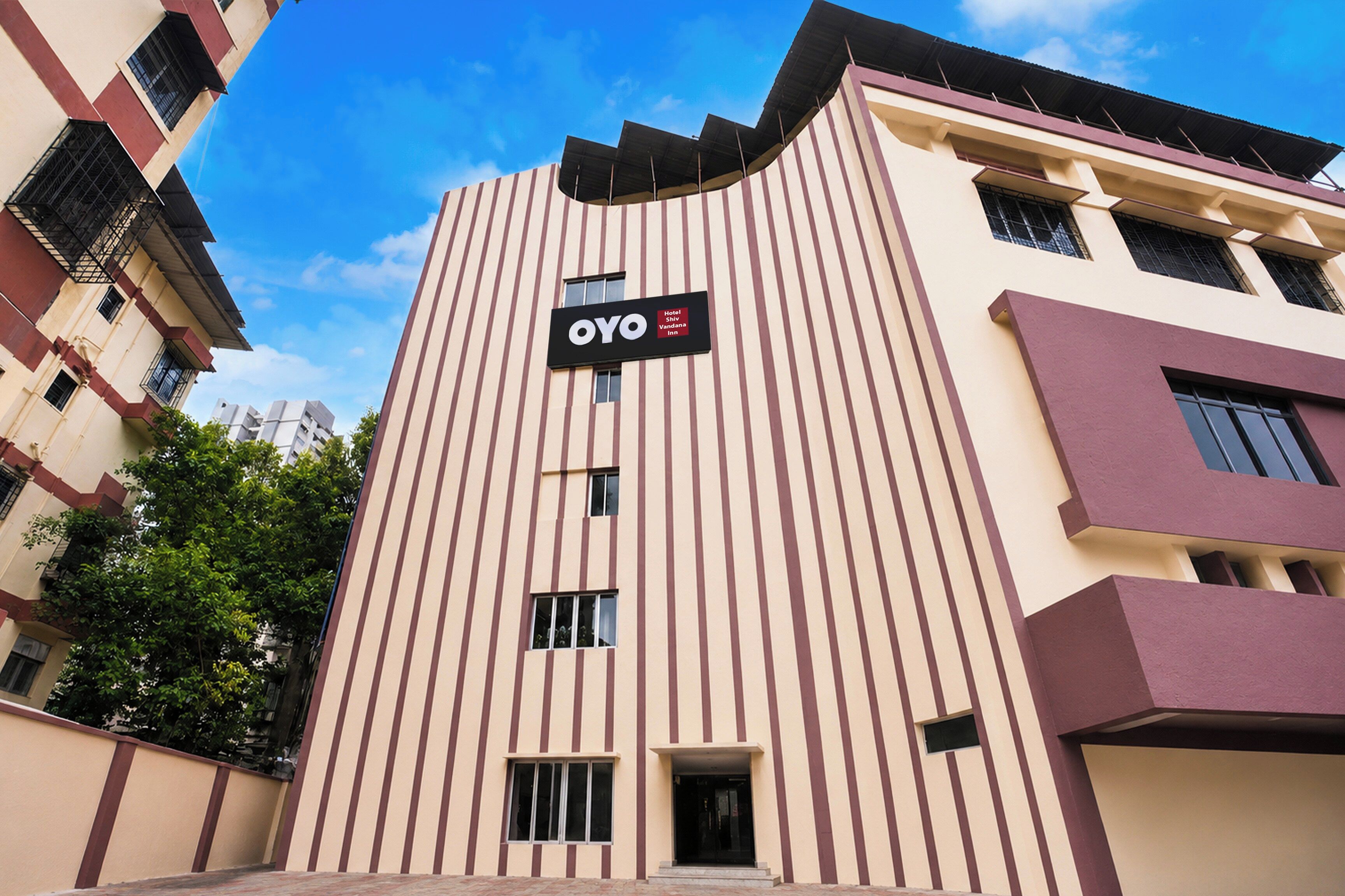 Un edificio de hotel con fachada a rayas verticales, un cartel que indica que es un Hotel OYO y un cielo despejado al fondo.