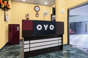 Una recepción con un cartel que dice 'OYO' en el vestíbulo de un hotel, que tiene piso de mármol, un extintor, un reloj y un ventilador de pared.