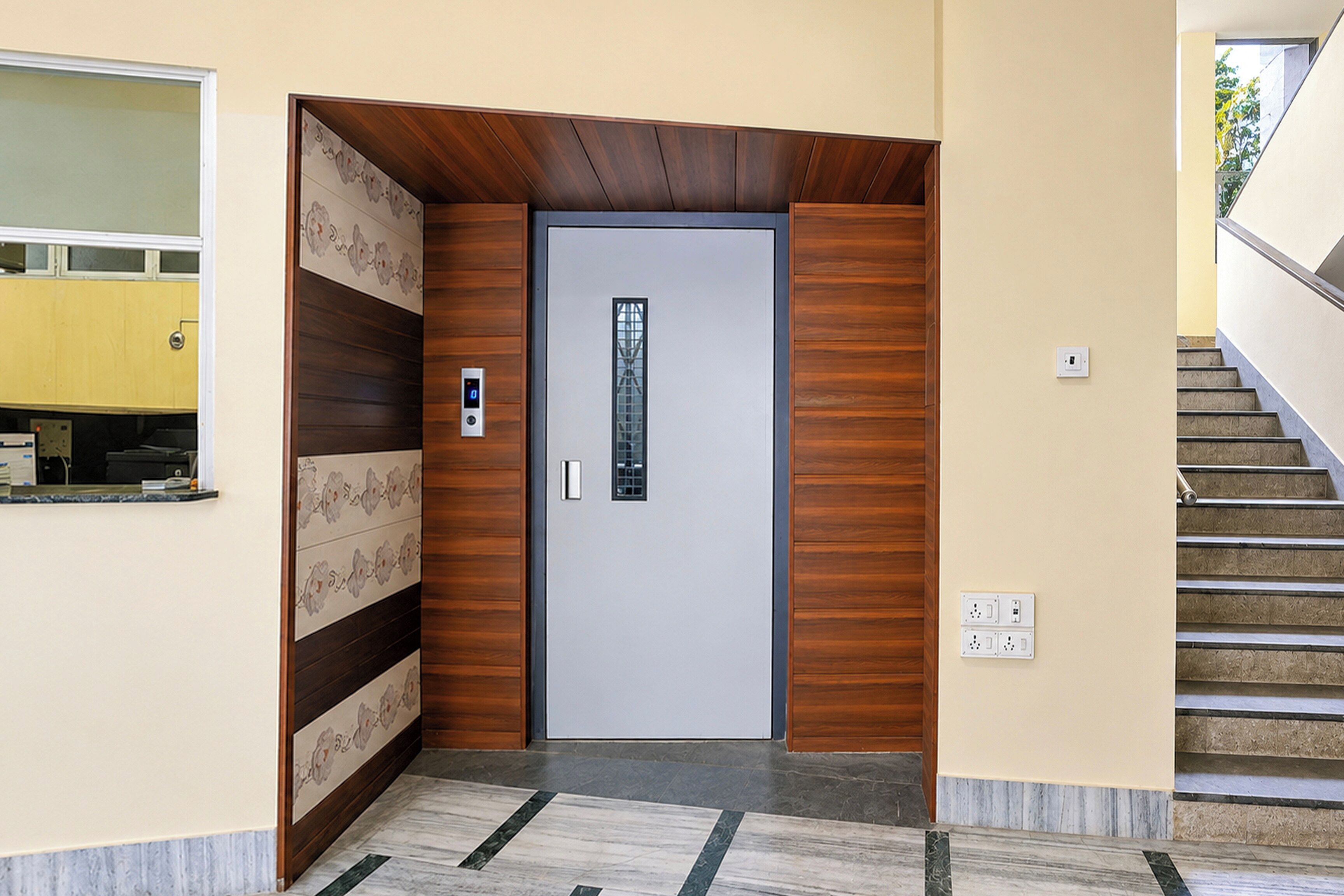 Una entrada moderna con diseño de paneles de madera, una puerta con panel de vidrio y una escalera a la derecha.