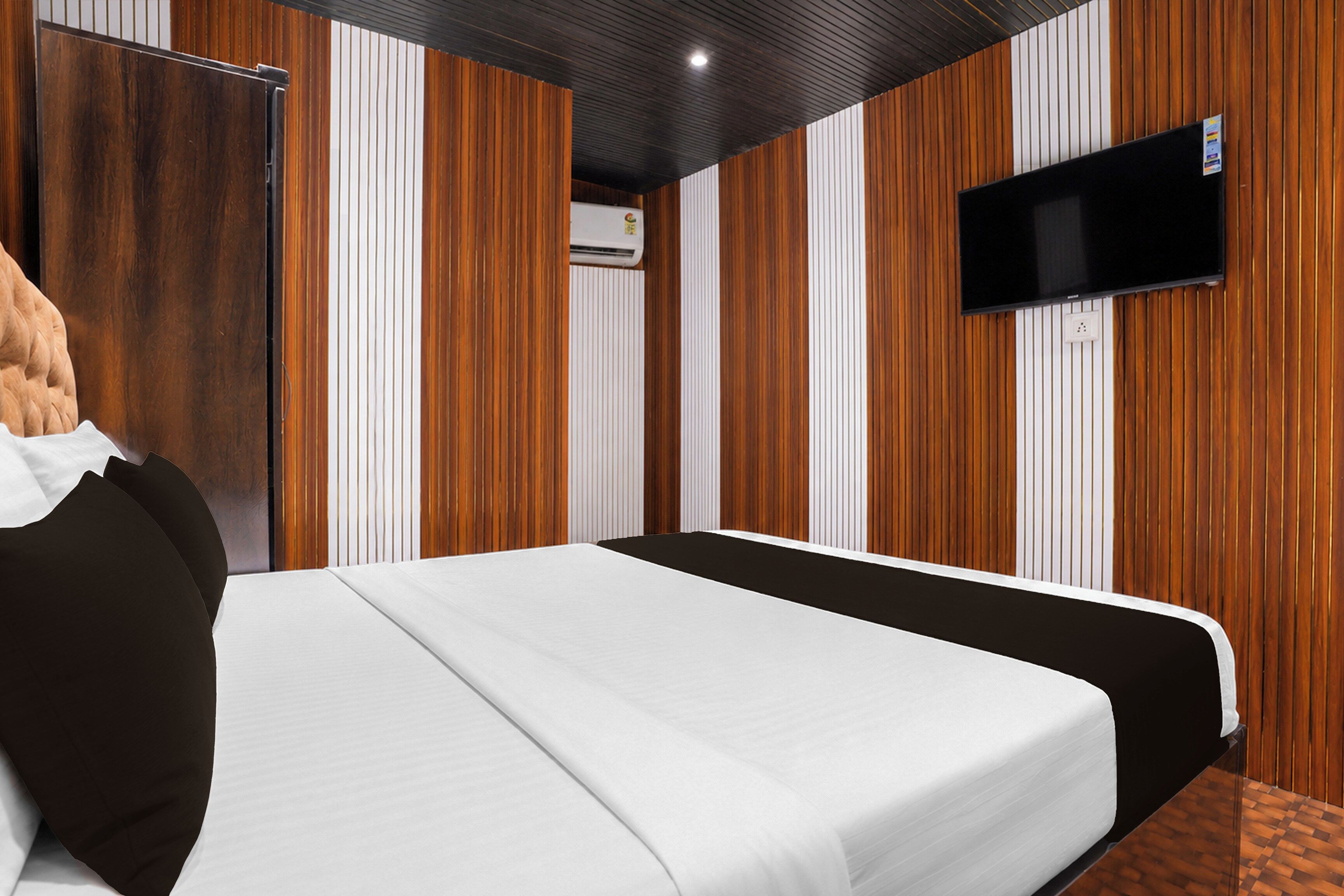 Habitación de hotel con una cama, un televisor montado en la pared y paneles de madera en las paredes.