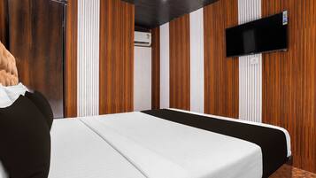 Habitación de hotel con una cama, un televisor montado en la pared y paneles de madera en las paredes.