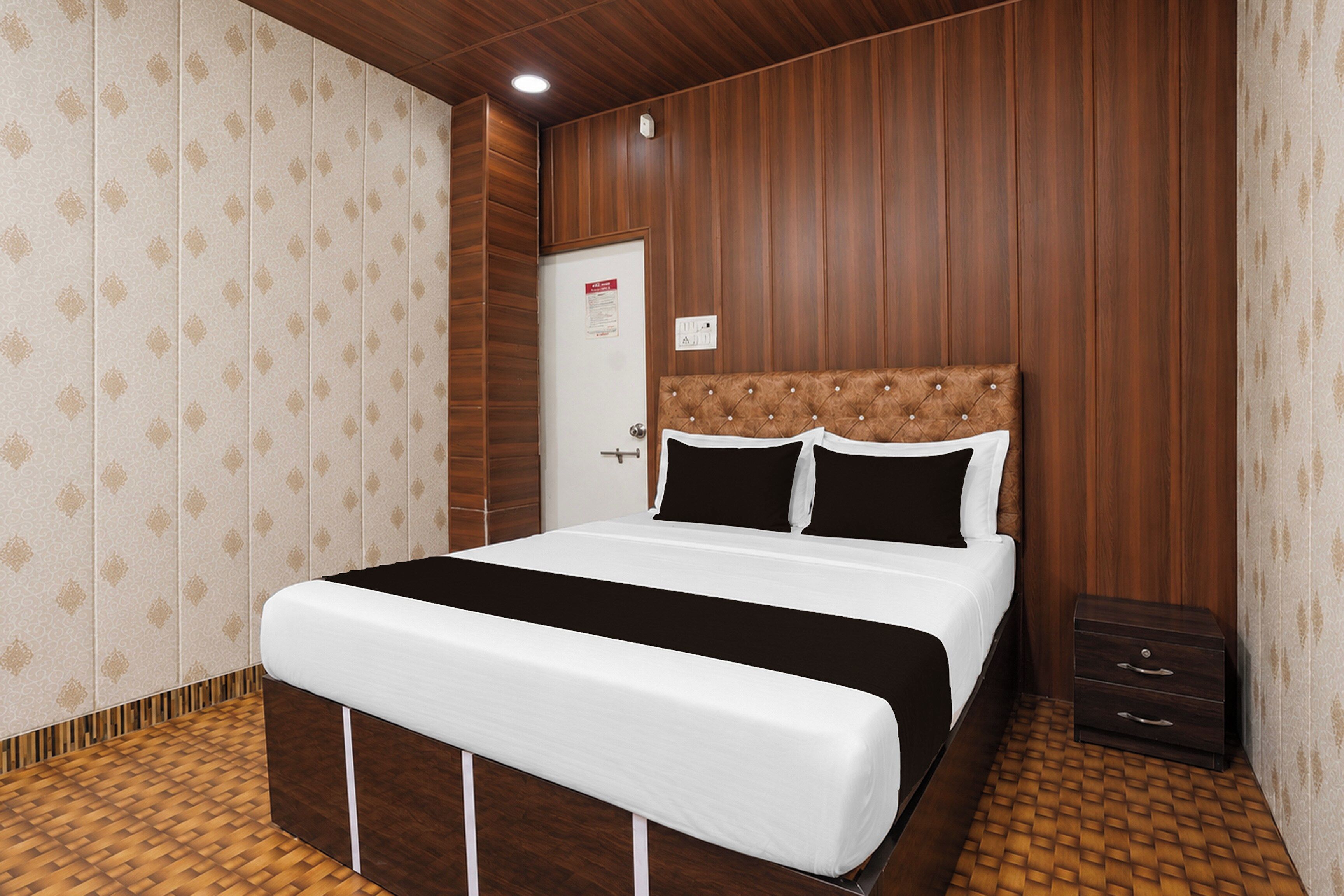 Une chambre d’hôtel avec un lit, une tête de lit en bois, une porte et une petite table de chevet.
