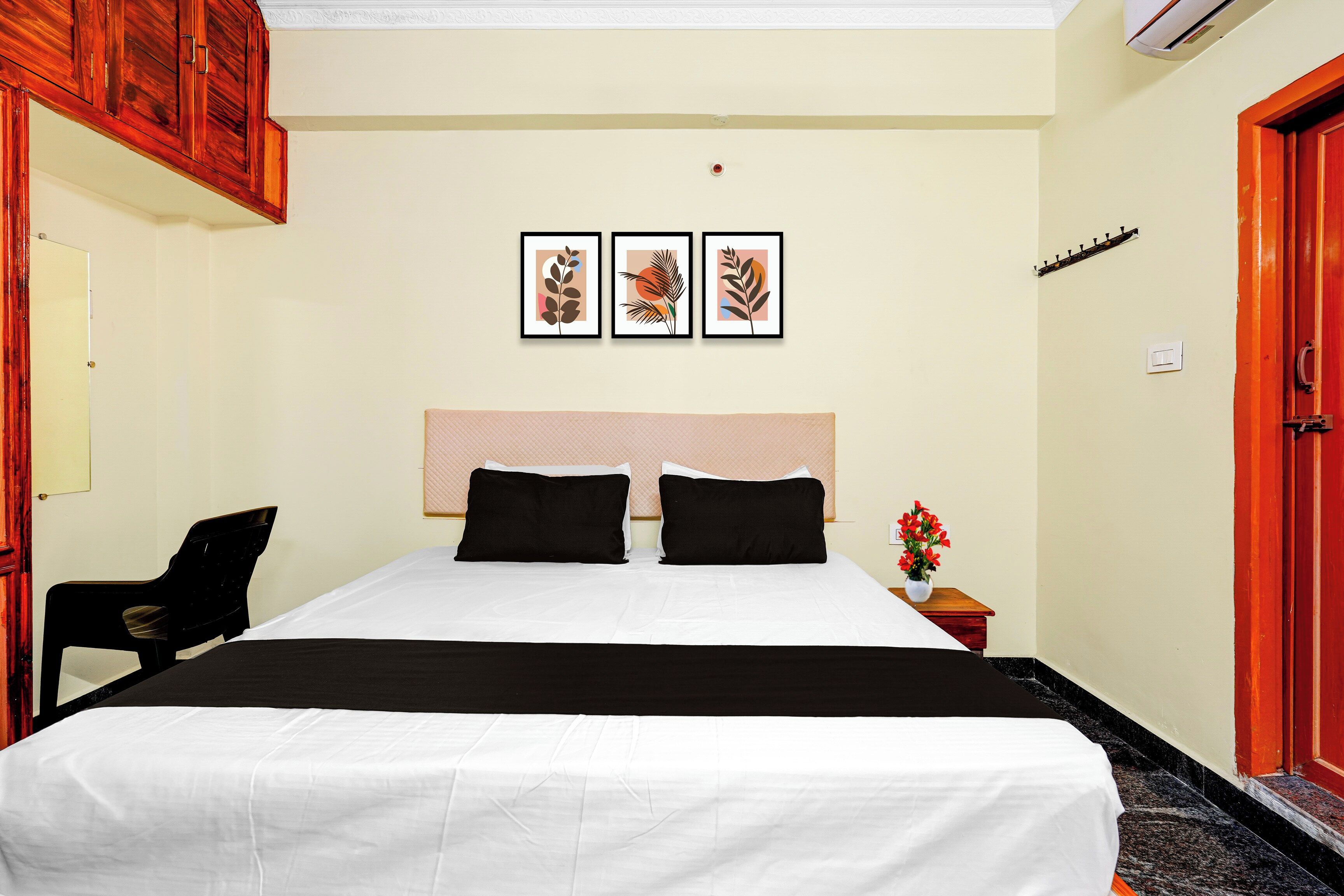 Une chambre d’hôtel avec un lit, une chaise, une table de chevet ornée d’un vase de fleurs et trois tableaux encadrés accrochés au mur.