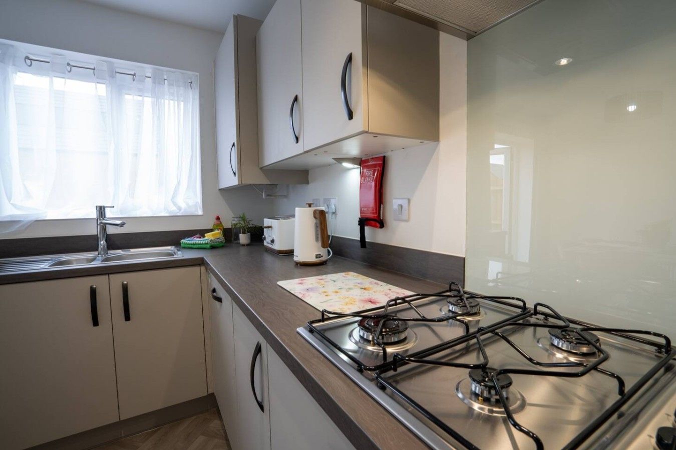 Une cuisine moderne équipée d’une cuisinière à gaz, d’un évier et d’une fenêtre ornée de rideaux légers.