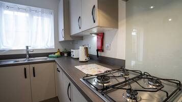 Une cuisine moderne équipée d’une cuisinière à gaz, d’un évier et d’une fenêtre ornée de rideaux légers.