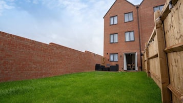 Een gebouw van baksteen met een plat dak, een gazon en een houten omheining.