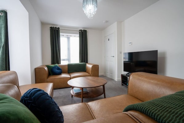 A modern living room with leather sofas, a round coffee table, and a flat-screen TV. - Peak Avenue Retreat - Dog Friendly with Garden! (Derbyshire)