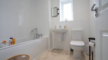 Ein Badezimmer mit Badewanne, Waschbecken, Toilette und einem kleinen Fenster.