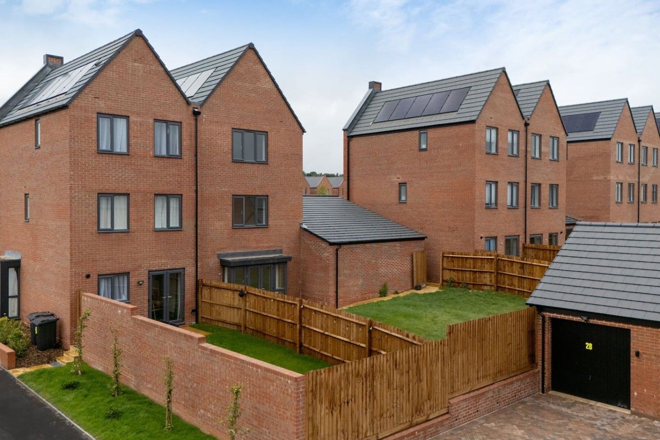 A residential building with multiple brick houses, each with a pitched roof and solar panels.