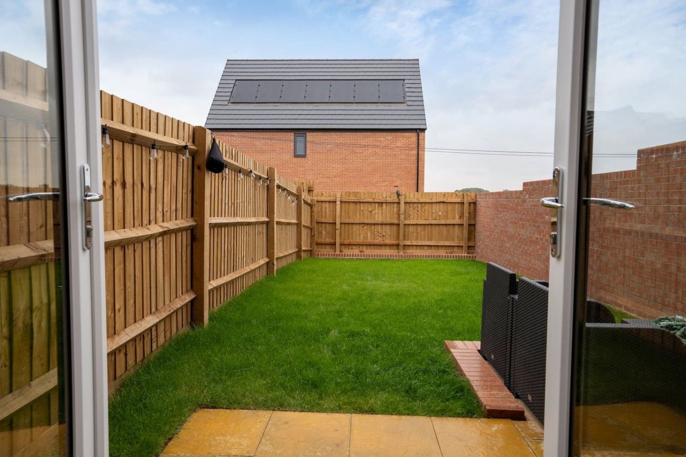 Un jardin avec une pelouse verdoyante, une clôture en bois et un mur en briques.