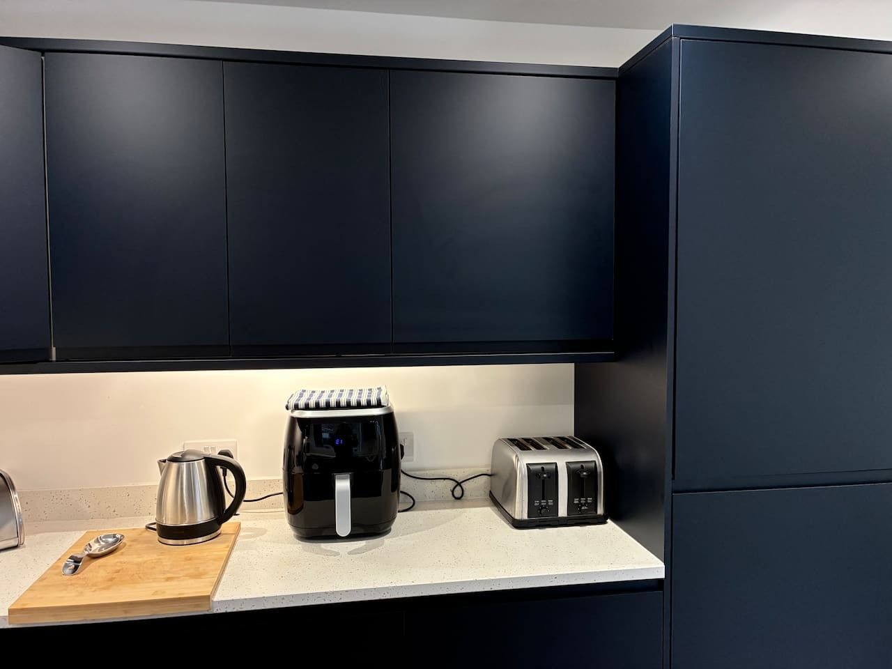 Eine Küche mit dunklen Schränken, einer Kaffeemaschine, einem Toaster und einem Wasserkocher auf der Arbeitsplatte.