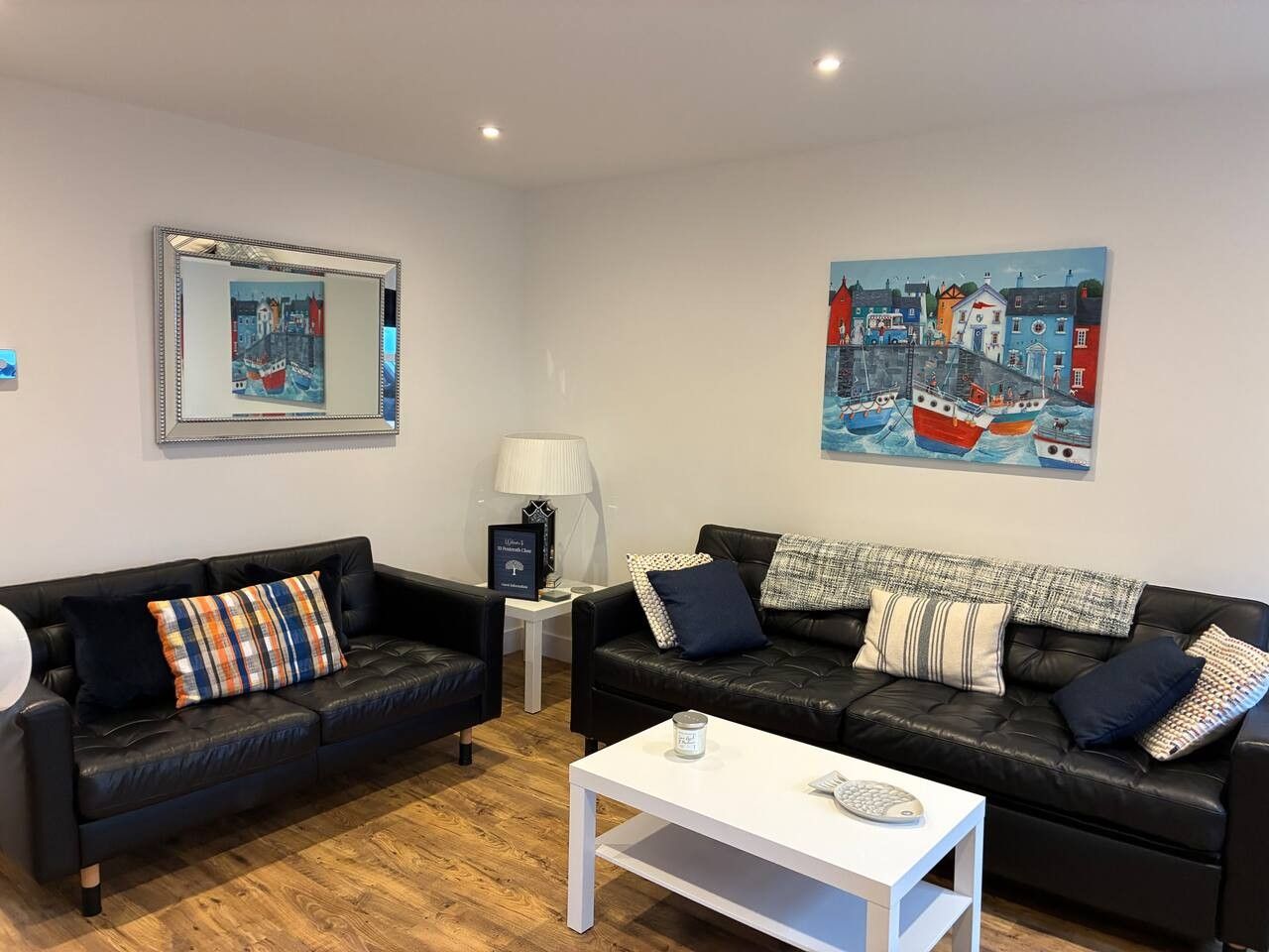 A modern living room with two black leather sofas, a white coffee table, and two paintings on the walls.