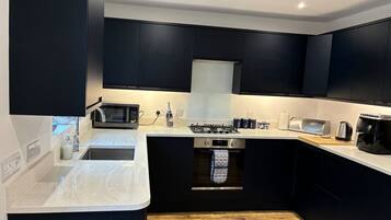 Una cocina moderna con armarios oscuros, un lavamanos de acero inoxidable, un microondas, un horno empotrado y una cafetera.