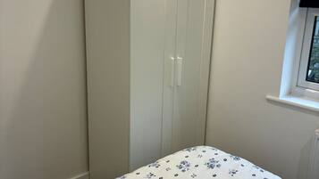 A bedroom with a single bed, a wardrobe, and a window.