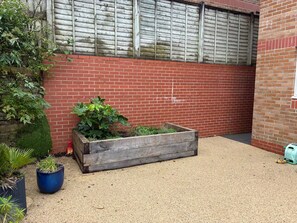 Un espace jardin aménagé avec un parterre surélevé en bois, un sol recouvert de gravier et un mur en briques.