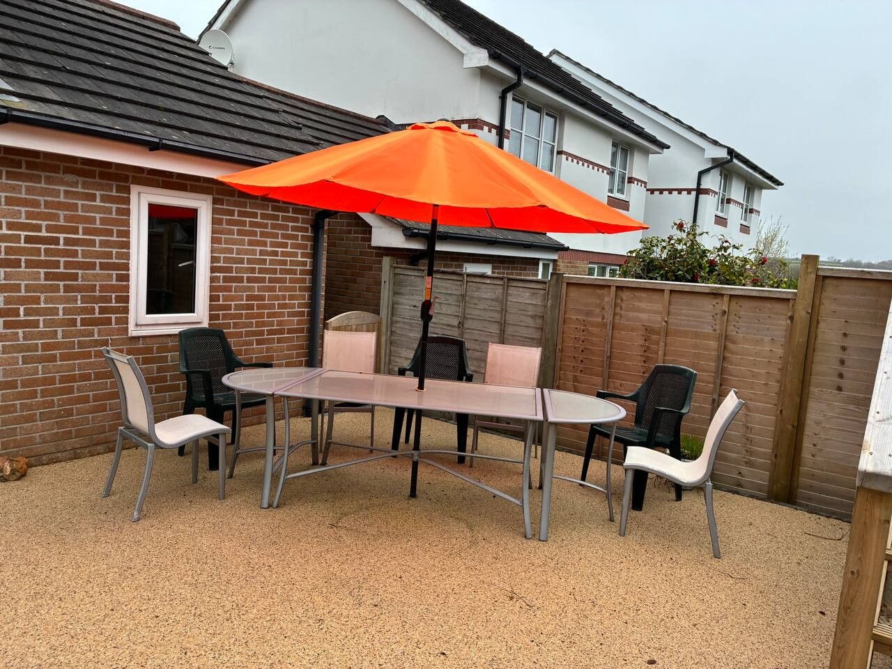 A patio with a table and chairs, an orange umbrella, and a brick wall.