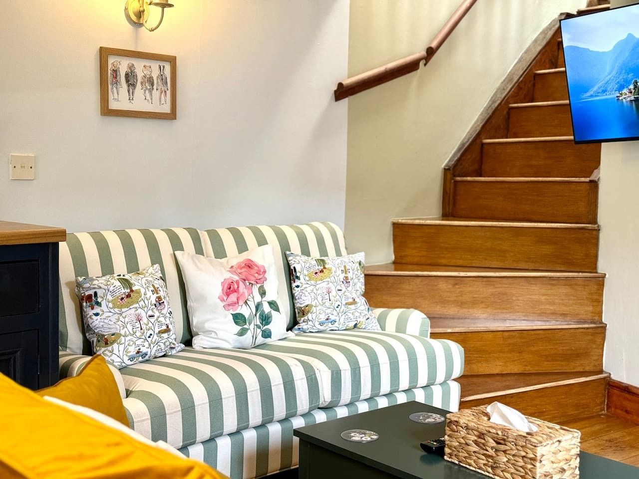 A living room with a striped sofa, a coffee table, and a television on a wooden staircase.