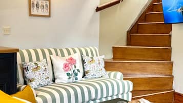 A living room with a striped sofa, a coffee table, and a television on a wooden staircase.