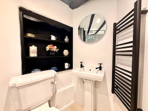 A bathroom with a toilet, sink, and a shelf with decorative items. - Wind in the Willows Moreton in Marshes (Gloucestershire)