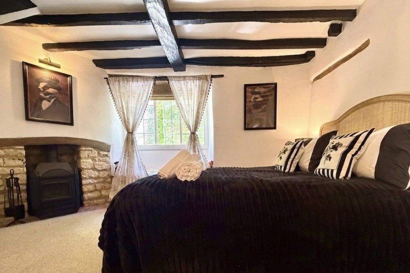 A bedroom with a stone fireplace, a bed with black bedding, and a window with curtains.