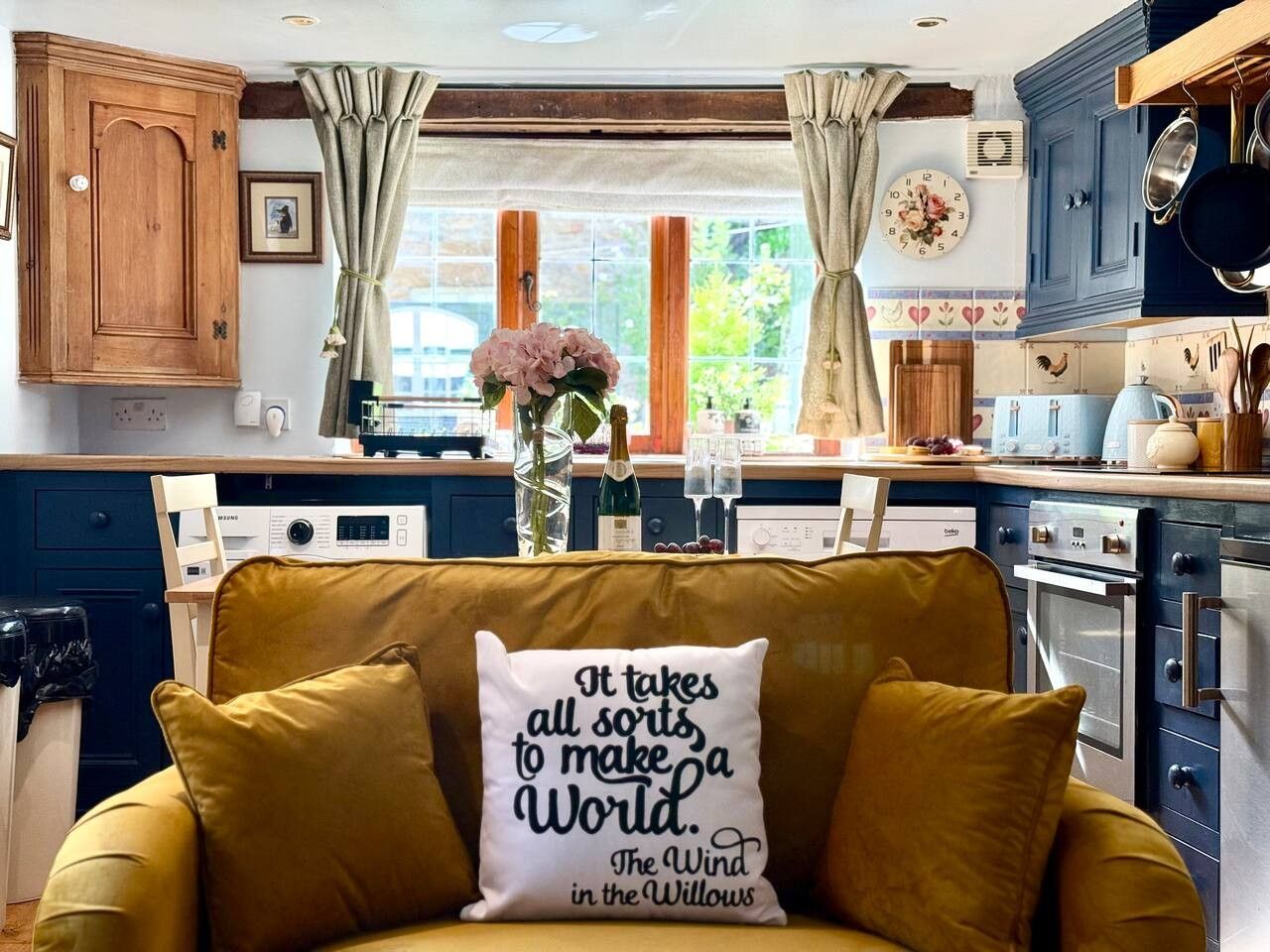 A cozy kitchen with a yellow sofa, a clock, and a window with curtains.