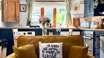 A cozy kitchen with a yellow sofa, a clock, and a window with curtains.
