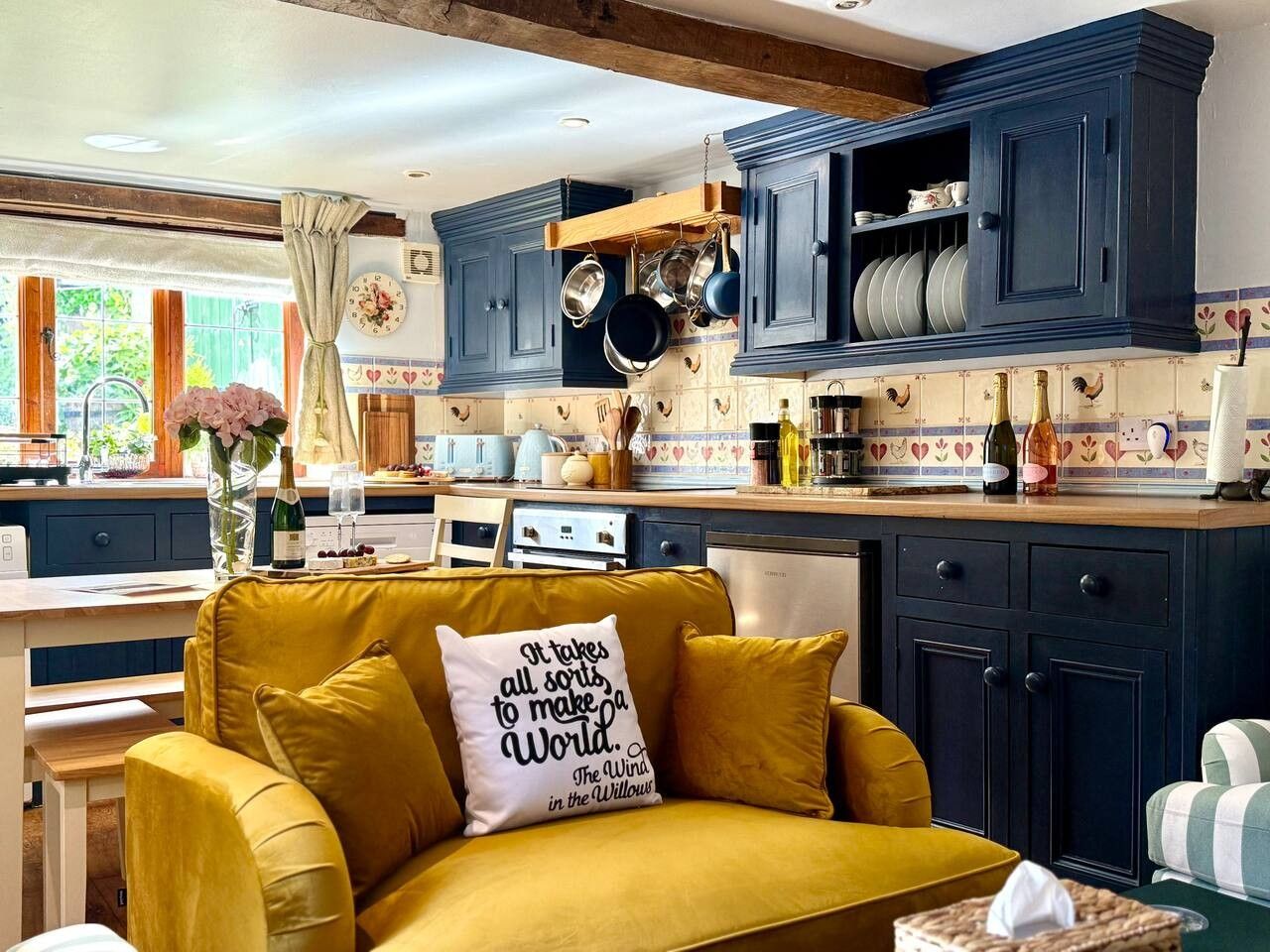 A kitchen with blue cabinets, a yellow sofa with a pillow, and a window with curtains.