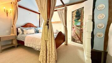 A bedroom with a four-poster bed, a nightstand, and a view of a garden through a window.