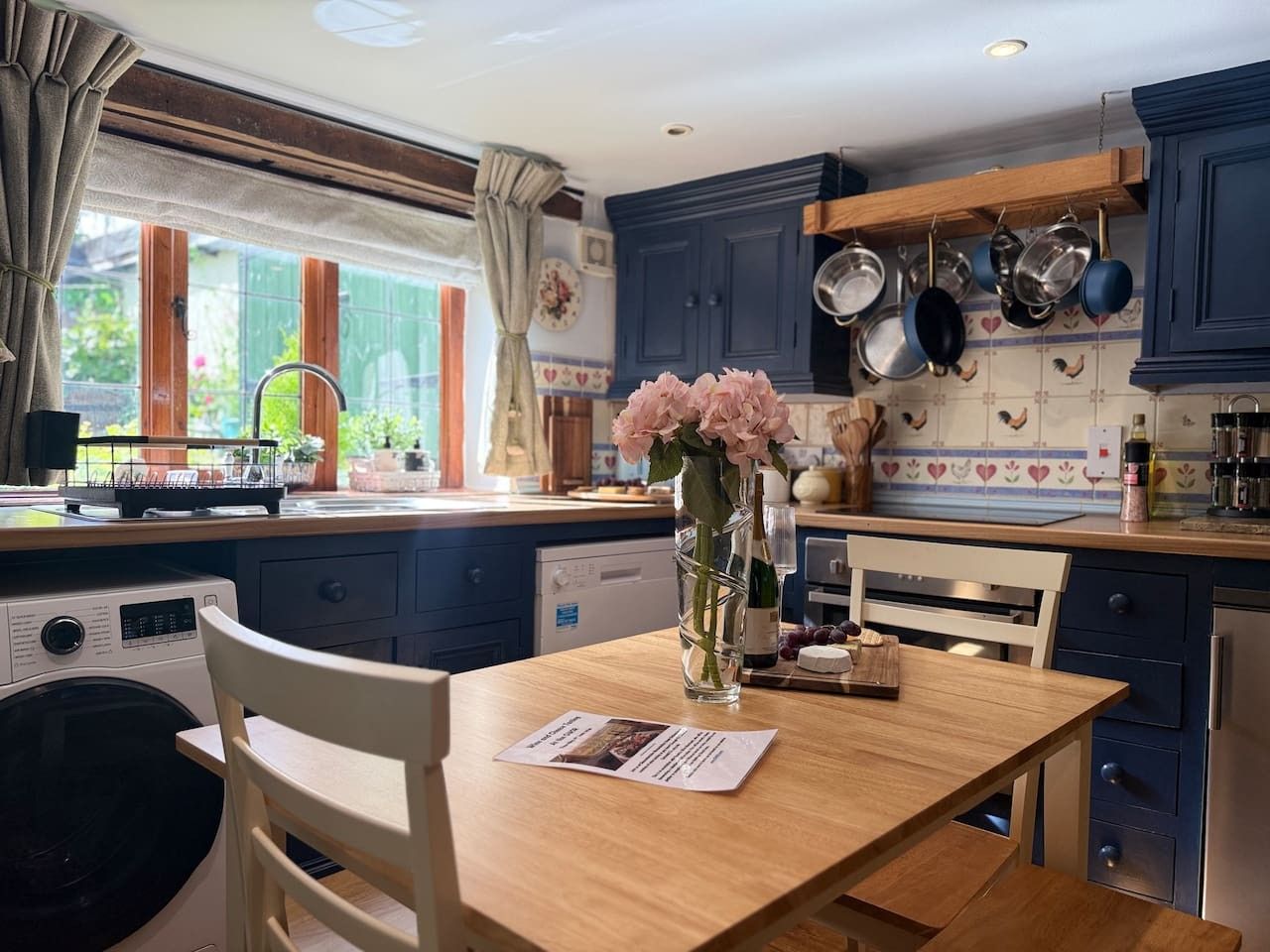 A kitchen with a wooden table, chairs, a vase with flowers, and a washing machine.