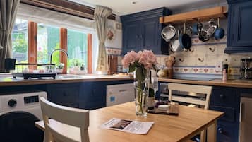 A kitchen with a wooden table, chairs, a vase with flowers, and a washing machine.