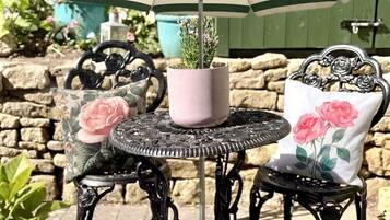 A round metal table with a potted plant, two chairs with floral cushions, and a striped umbrella.