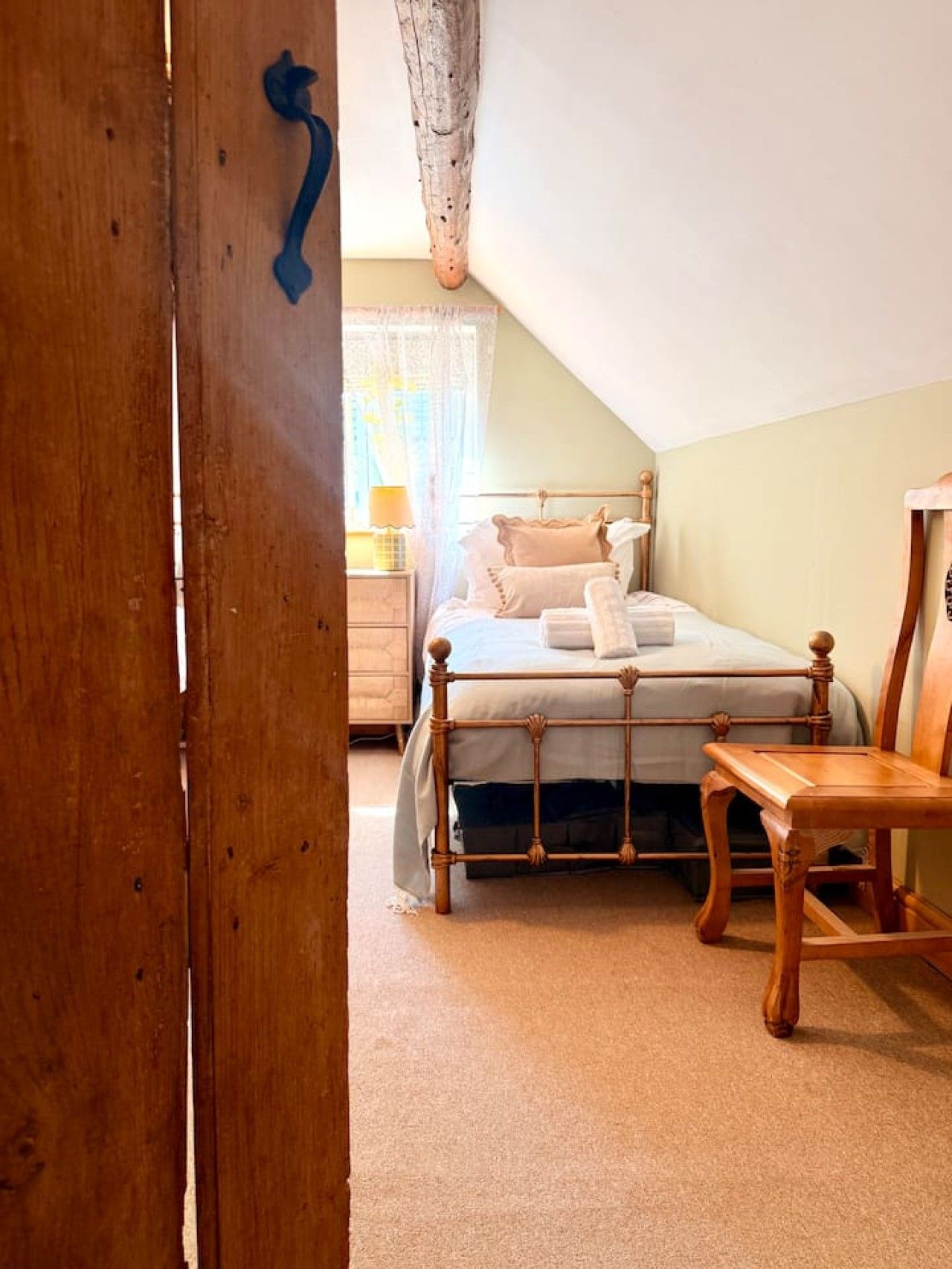 A bedroom with a wooden bed frame, a bedside table, and a chair.