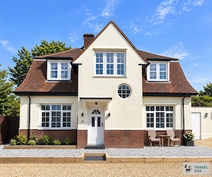 A two-story house with a symmetrical facade, a central entrance with a white door, and a small porch with seating. - Sea Marge Cottage with off-road parking! (Overstrand)