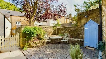 A courtyard with a stone wall, a blue shed, and a tree with red leaves.