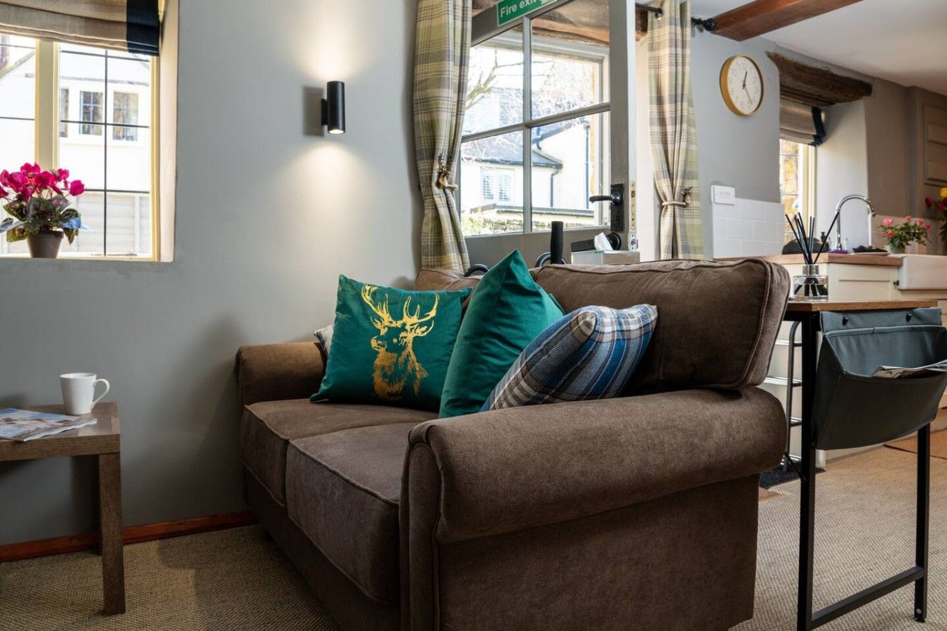 A cozy living room with a brown sofa, a small table with a cup, and a window with curtains.