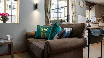 A cozy living room with a brown sofa, a small table with a cup, and a window with curtains.
