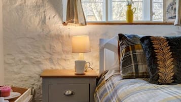 A bedroom with a bed, a nightstand with a lamp, a window with curtains, and a view of trees outside.