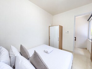 Una camera d'albergo con un letto, cuscini, un armadio e una porta che dà su un'altra stanza.