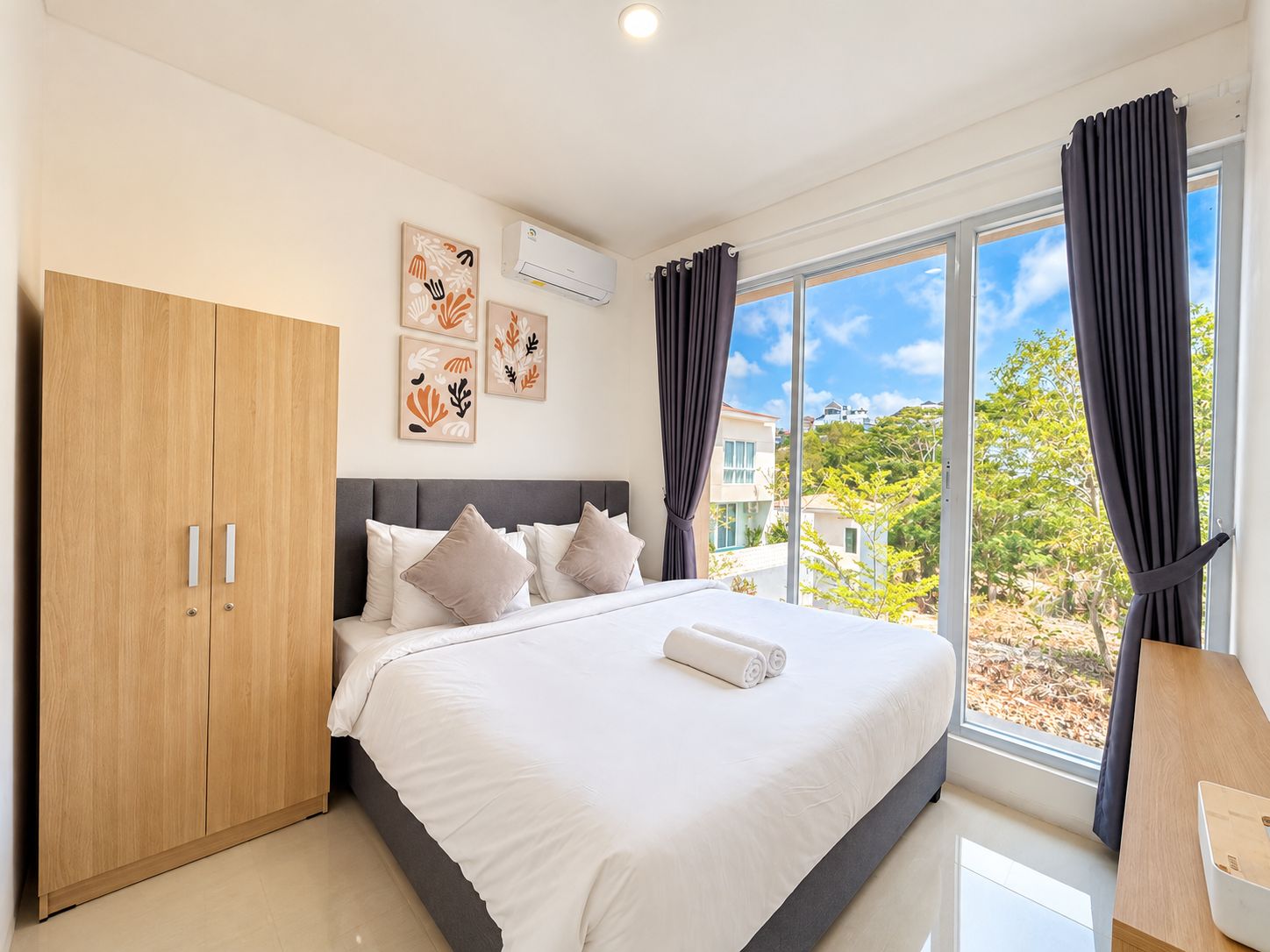 A bedroom with a bed, a wardrobe, a window with curtains, and artwork on the wall.