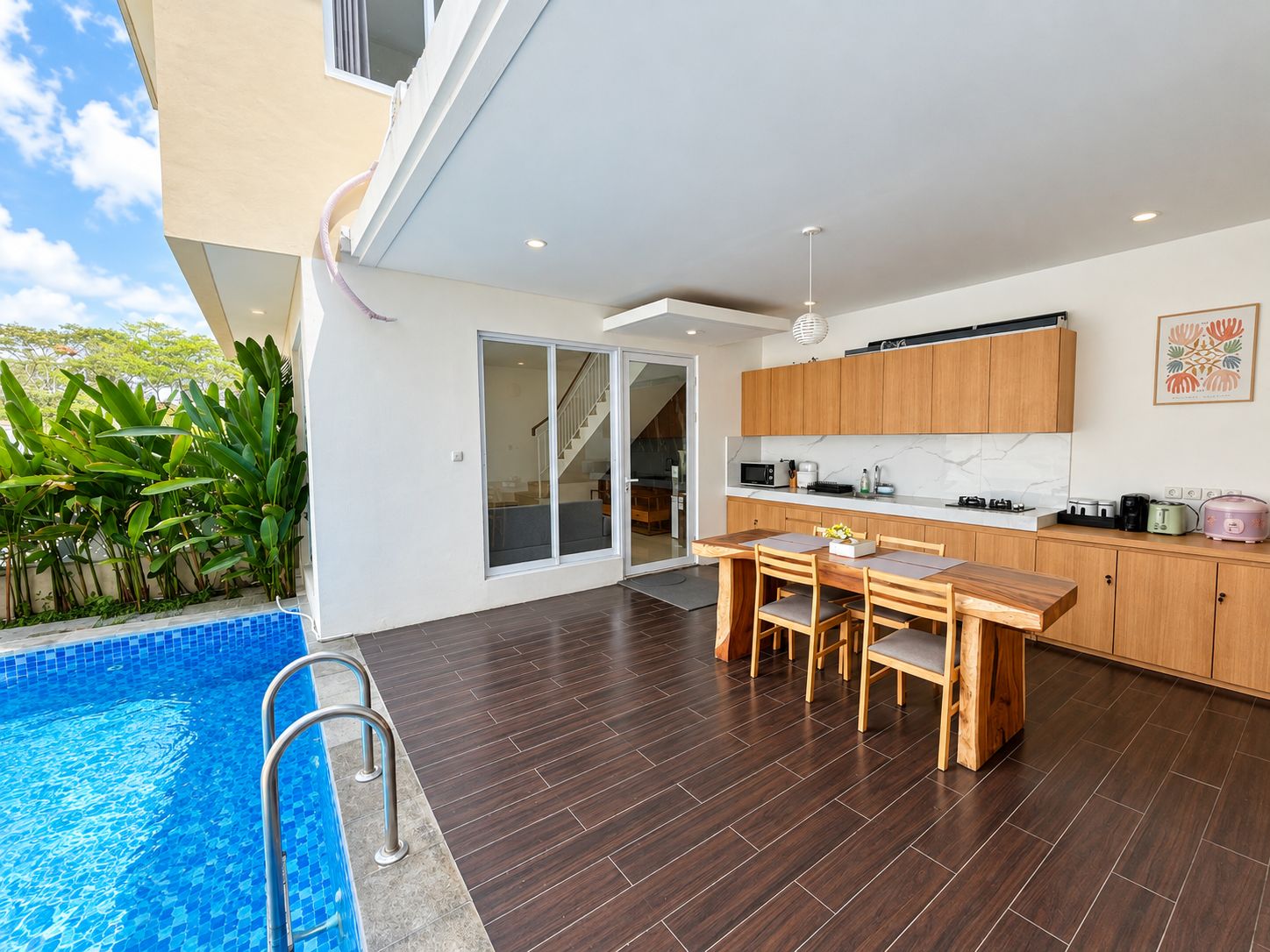 A modern kitchen with wooden cabinets, a dining area with a table and chairs, and a poolside area with a ladder.