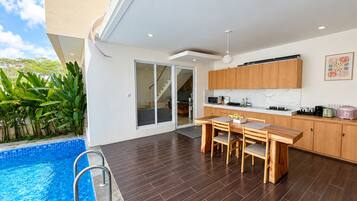 A modern kitchen with wooden cabinets, a dining area with a table and chairs, and a poolside area with a ladder.