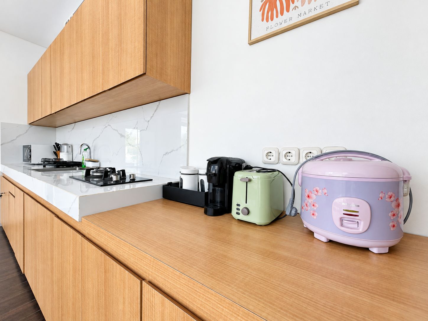 A modern kitchen with a marble countertop, wooden cabinets, a coffee maker, a toaster, and a pink rice cooker.