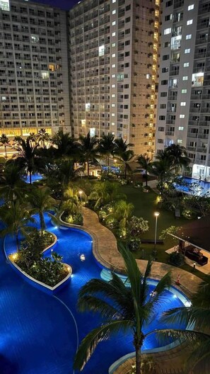 A multi-story hotel with a swimming pool surrounded by palm trees and well-lit pathways. - 1 BR Unit near MOA SMX WTC NAIA Manila Bay (Pasay City)