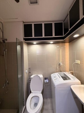 Een kleine badkamer met toilet, wasmachine en douche.